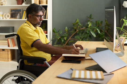 Developer in wheelchair writing script on computer at home office
