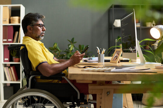 Coder with disability checking smartphone at workplace - Powered by Adobe