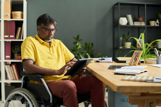 Office employee in wheelchair using tablet at desk