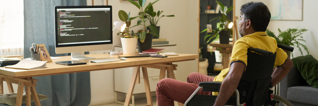 Man in wheelchair coding at home office with senior woman nearby