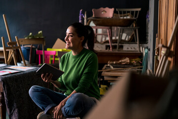Woman in a green sweater sitting in an art studio holding a tablet
