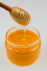 Close-up of a wooden spoon over a glass jar with yellow liquid honey nectar, from which honey drips down in a trickle on a white background. The concept of healthy eating, healthy sweet foods, diet