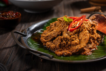 A plate of beef rendang, a rich Indonesian dish cooked in coconut milk and spices, served on a banana leaf. Garnished with red chili slices, this festive meal is popular during Eid celebrations