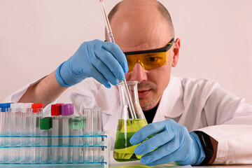 Scientist wearing protective glasses and gloves adding reagent with a pipette to an erlenmeyer...
