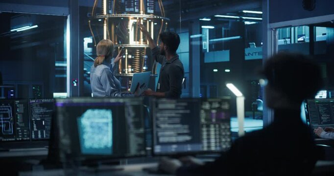 Portrait of a Middle Aged Caucasian Female Team Leader and Young Indian Engineer Talking in an Office with a Futuristic Quantum Computer Device. Specialists Discussing Research Developments