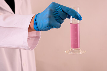 Scientist wearing blue gloves holding graduated cylinder containing pink liquid during experiment...