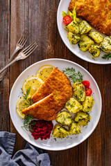 Breaded fried pork chop with boiled potatoes and beets on wooden table	