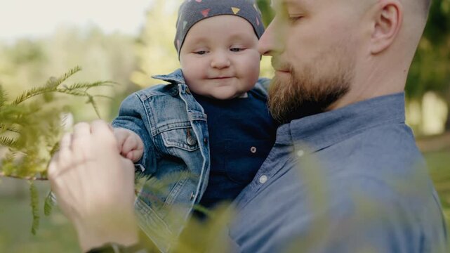 A tender moment captured as a father holds his baby boy, both enjoying a quiet day in the park. Perfect for expressing familial love and bonding. Father Holding Smiling Baby Boy in Peaceful Park