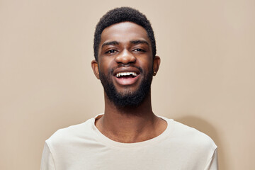 Happy young man smiling in a neutral toned shirt against a warm beige background, representing...