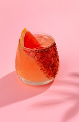 Cold and refreshing cocktail with ice garnished grapefruit slice stands on pink background. Summer non-alcoholic cocktail with juice and soda. Hard light, bar menu.