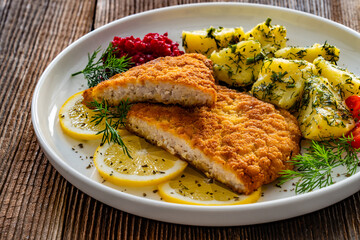 Breaded fried pork chop with boiled potatoes and beets on wooden table	