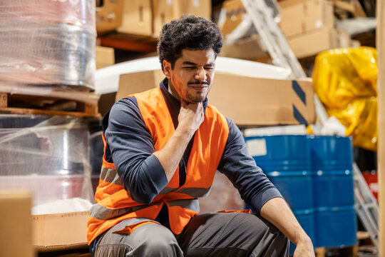 An ill interracial warehouseman with sore throat frowning.