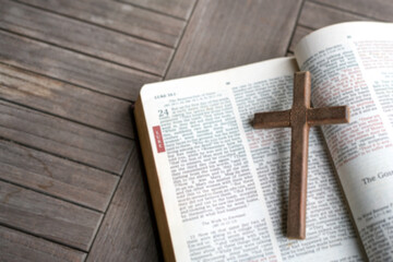 Wooden crucifix cross on top of an open Holy Bible. High angle view. Defocused text.