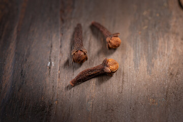 Three dried cloves placed on a rustic wooden table. A warm, aromatic spice commonly used in Indonesian cuisine, enhancing the flavor of Eid dishes and festive meals with its distinct, rich