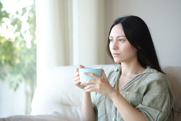 Serious asian woman drinking and contemplating in a house