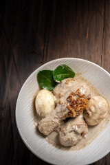 Opor ayam, a rich chicken dish in coconut sauce with eggs, shallots, and ketupat. A spicy and creamy meal for Eid, served on a wooden table with chili and kaffir leaves in the background