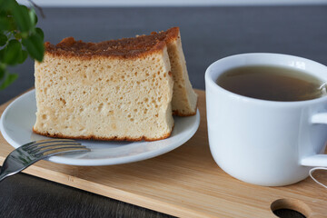 A cup of tea and a slice of castella muffin on a wooden board, selective focus.