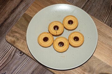 Five round cookies with golden edges sit on a light plate, each featuring a dark chocolate dot in...