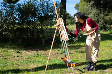 Latin woman artist painting in a public park on a sunny day