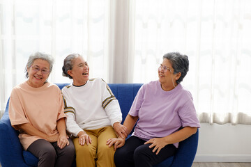 Three Asian senior women laughing together on a cozy couch, enjoying friendship, happiness, and a...