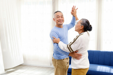 Asian senior couple dancing happily in a bright home, enjoying an active lifestyle, love, and togetherness. Perfect concept for aging gracefully, wellness, retirement, romance, and happiness.