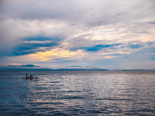 Obraz premium Two people enjoy a peaceful kayaking experience under a dramatic, cloudy sunset sky. the expansive ocean reflects the changing hues, creating a calming atmosphere. the horizon features distant