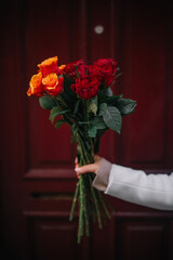 Holding a vibrant bouquet of roses against a rich red background