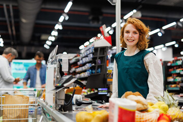 Smiling cashier working at checkout counter in supermarket