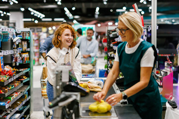 Cashier scanning groceries of smiling customer at supermarket checkout