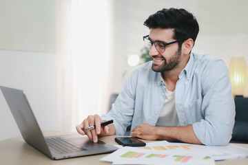 Fototapeta premium Man working on laptop at home with happy smile with cup of coffee and documents