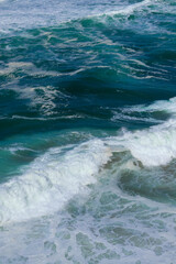 Fototapeta premium Ocean waves in Portugal. Blue and green water with white foam moving in the Atlantic Ocean. The power and beauty of nature in motion.
