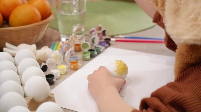 Young artist carefully painting easter eggs with yellow tempera color