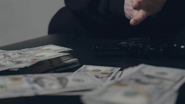 A gangster or thief sits with folded hands at a table with money and a gun. The concept of banditry, crime, mafia