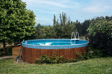 Above-ground backyard swimming pool surrounded by lush greenery, emphasizing outdoor leisure,...