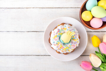 Traditional Easter cake decorated with sugar icing and sprinkles, with festive spirit decor and flower bouquet. Easter celebrations holiday table with pastel colored Easter eggs and bunny rabbits