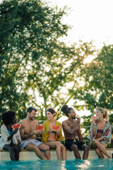 Friends eating watermelon by the poolside on summer vacation
