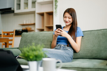Young asian woman relax on comfortable couch at home texting messaging on smartphone and tablet smiling girl