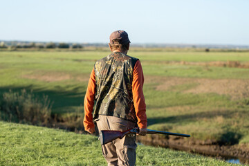 Mature hunter man holding a shotgun and walking through a field