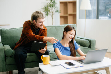 Two man and women enjoy remote work in a cozy living room, using a laptop while sipping coffee and...