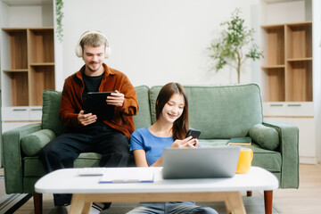 Two man and women enjoy remote work in a cozy living room, using a laptop while sipping coffee and...
