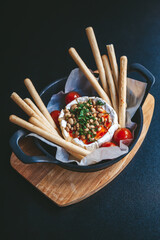 Baked cheese wheel topped with pine nuts, chopped herbs, and chili oil, surrounded by breadsticks...