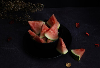 Top view of watermelon cut into pieces inside a black bowl on a dark background. Tropical fruit on a rustic background