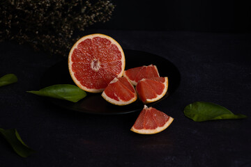 Halved grapefruit on a black plate on a dark background, citrus fruit with diuretic properties