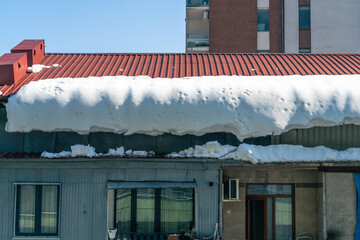 Heavy snow weighing down on a residential roof with large icicles and melting ice creating a...
