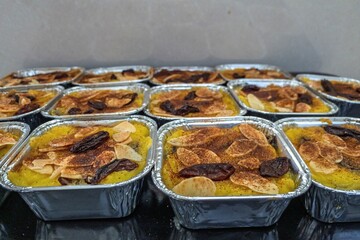 Delicious saffron-infused dessert topped with almonds, raisins, and cinnamon called Klappertaart or Klapertart in aluminum trays, perfect for catering, food photography, and culinary presentations.