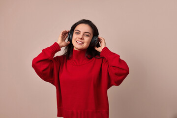 Happy girl wearing red sweater and headphones enjoying listening music on pink background.