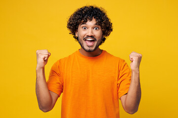 Young smiling fun happy Indian man he wear orange t-shirt casual clothes doing winner gesture...