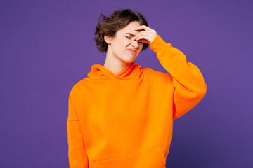 Young sick ill sad tired unhappy frustrated woman she wearing orange hoody casual clothes keep eyes closed rub put hand on nose isolated on plain purple background studio portrait. Lifestyle concept.