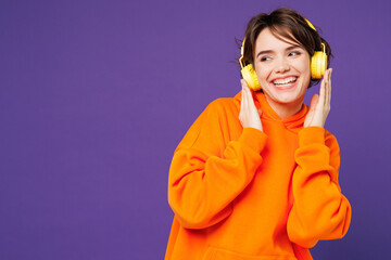 Young smiling happy Caucasian woman she wear orange hoody casual clothes listen to music in...