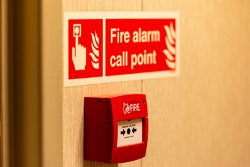 A red fire alarm call point mounted on the wall, designed for manual activation in case of fire.